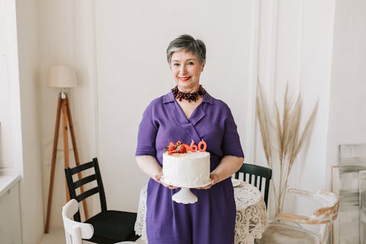 A cheerful senior woman holds a birthday cake with '60' candles indoors.