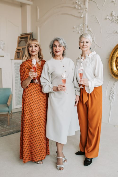 Free Three senior women in stylish dresses, holding champagne glasses and smiling indoors during a joyful celebration. Stock Photo