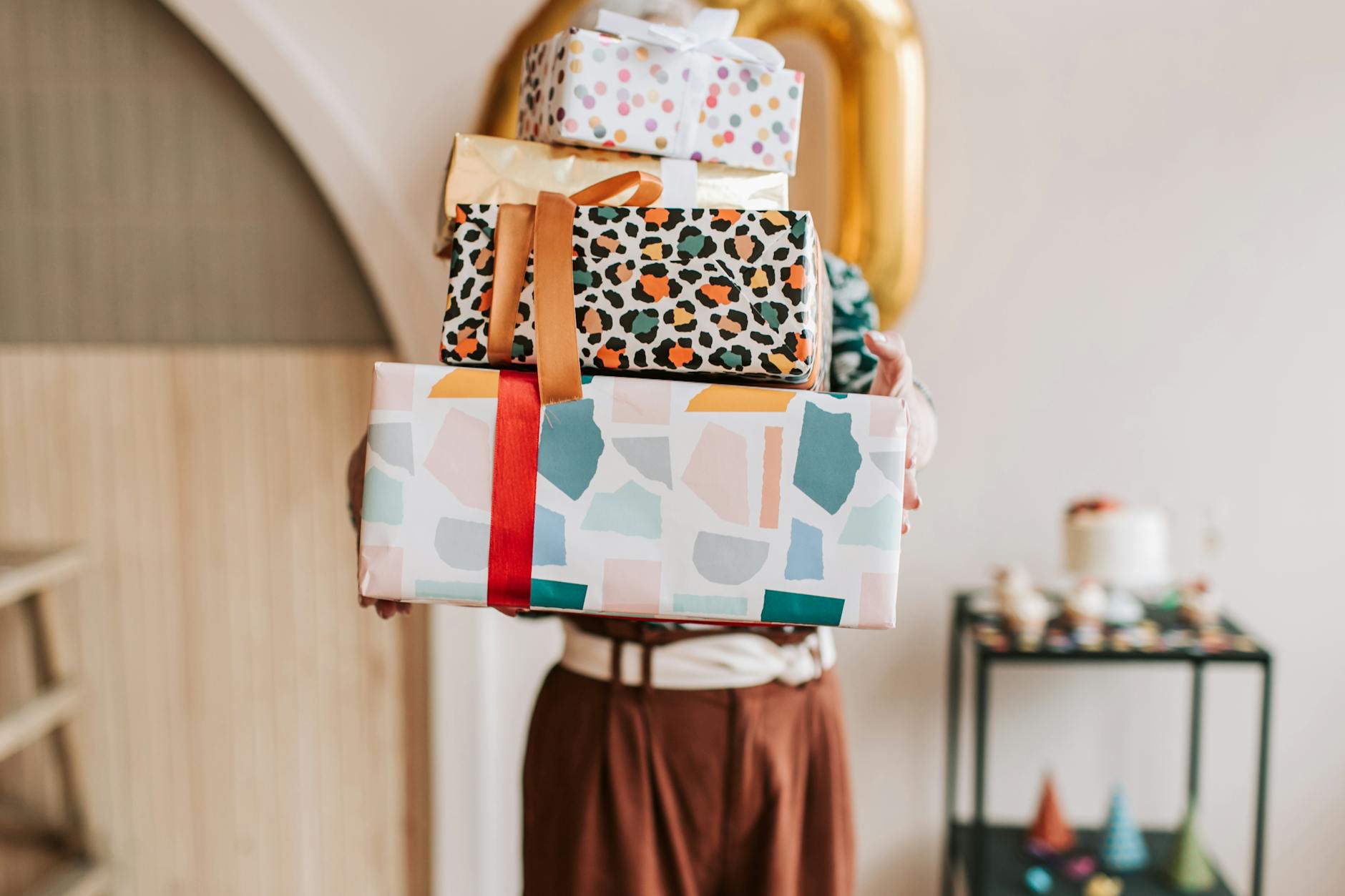 A person holding a stack of vibrant, wrapped gifts indoors, ready for a celebration.