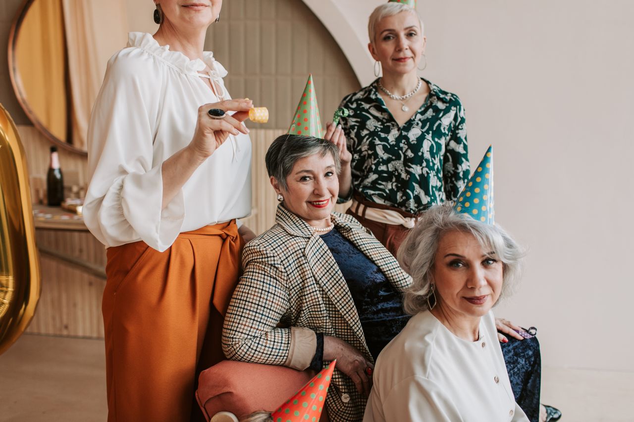 group of senior women celebrating indoors with party hats and decorati