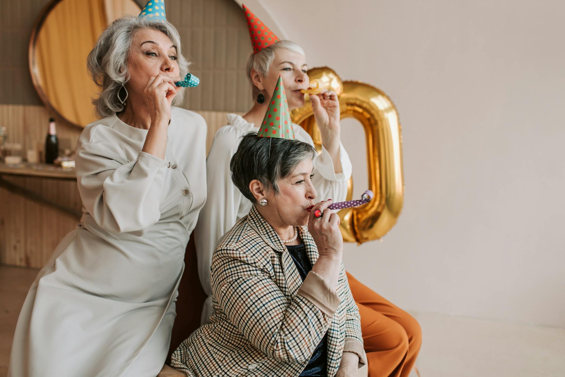 A joyful celebration with senior women in party hats blowing party blowers indoors.