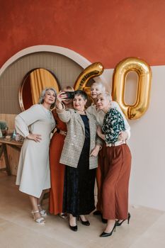 Elderly women celebrating a birthday indoors with balloons and taking a selfie.