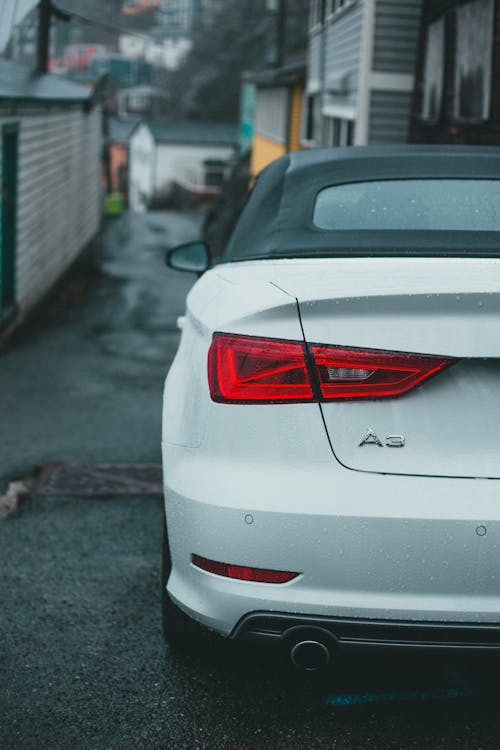 Rear bumper with trunk of modern automobile parked on asphalt walkway near shabby residential houses on street in suburb area