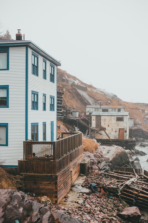 Residential buildings located on stony shore with stairs near grassy slope and river against cloudless sky in gloomy coastal area