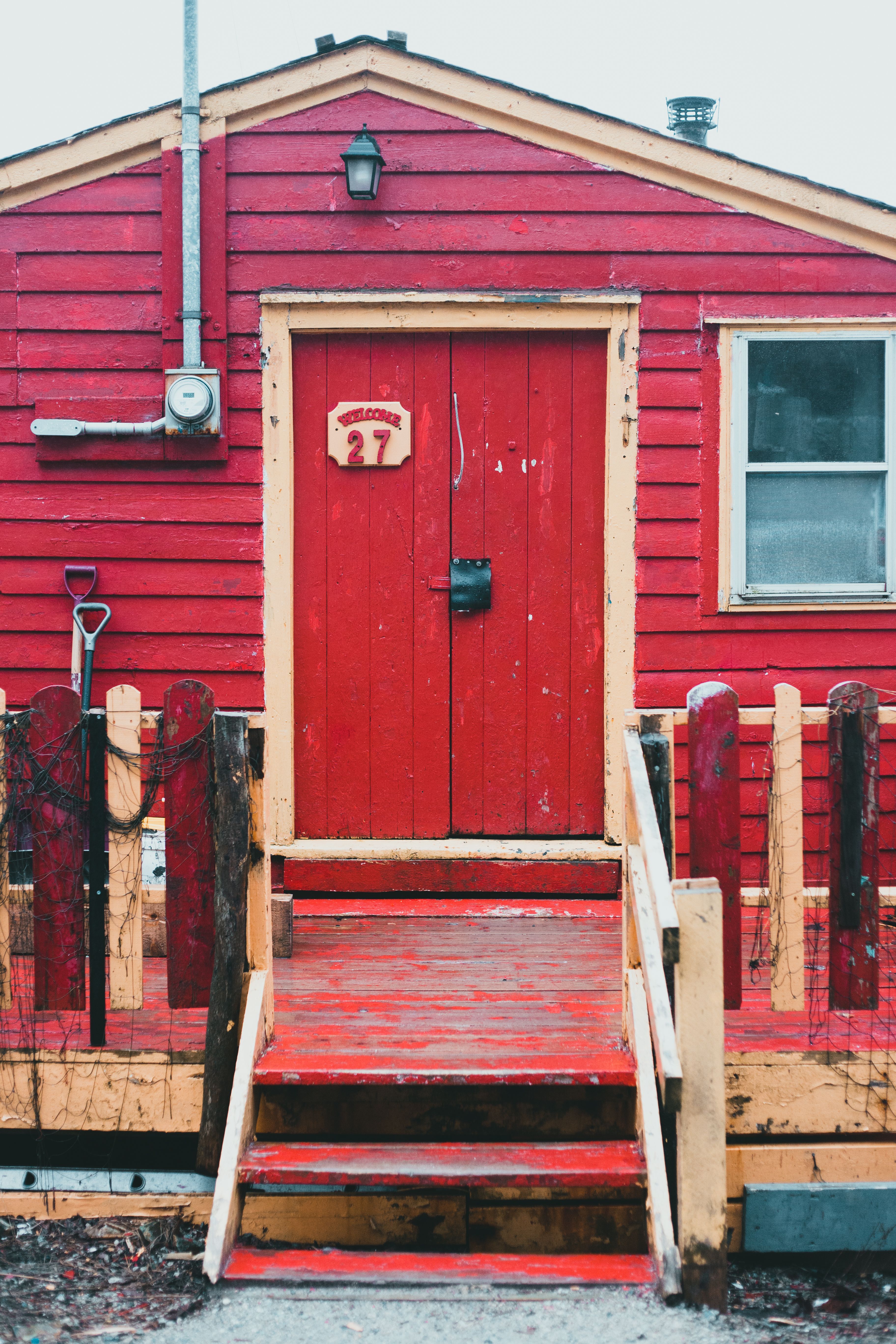 Facade of aged red shabby wooden building with door and steps near fence located on street in town against cloudless sky