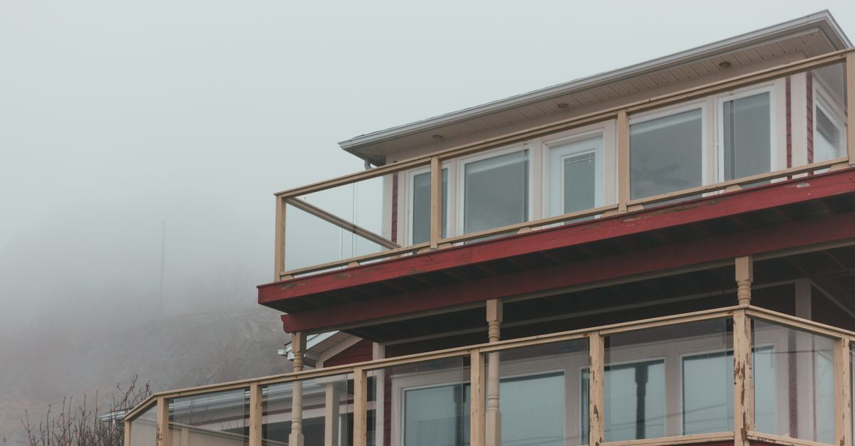 Weathered residential building with windows and terraces with fences located against thick misty sky in suburb area in overcast weather
