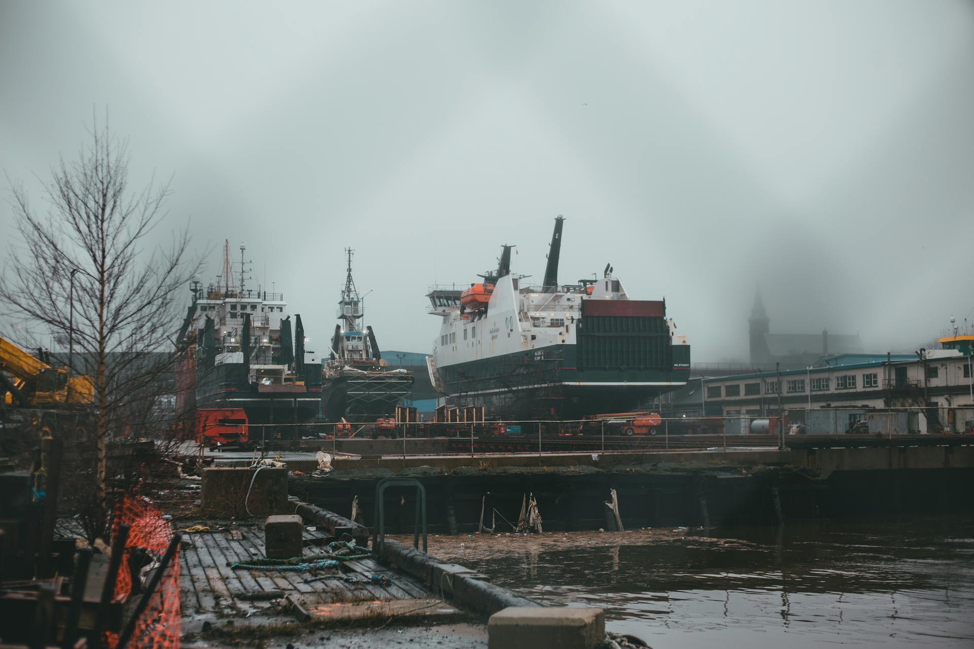 A misty harbor scene featuring docked ships in an industrial setting under a gloomy sky.