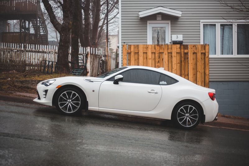White coupe parked kerbside on a wet residential street — photo by Erik Mclean on Pexels