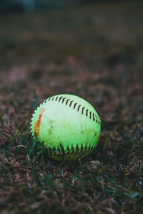 Free Close-up of a neon yellow softball resting on grass with shallow focus and depth of field. Stock Photo