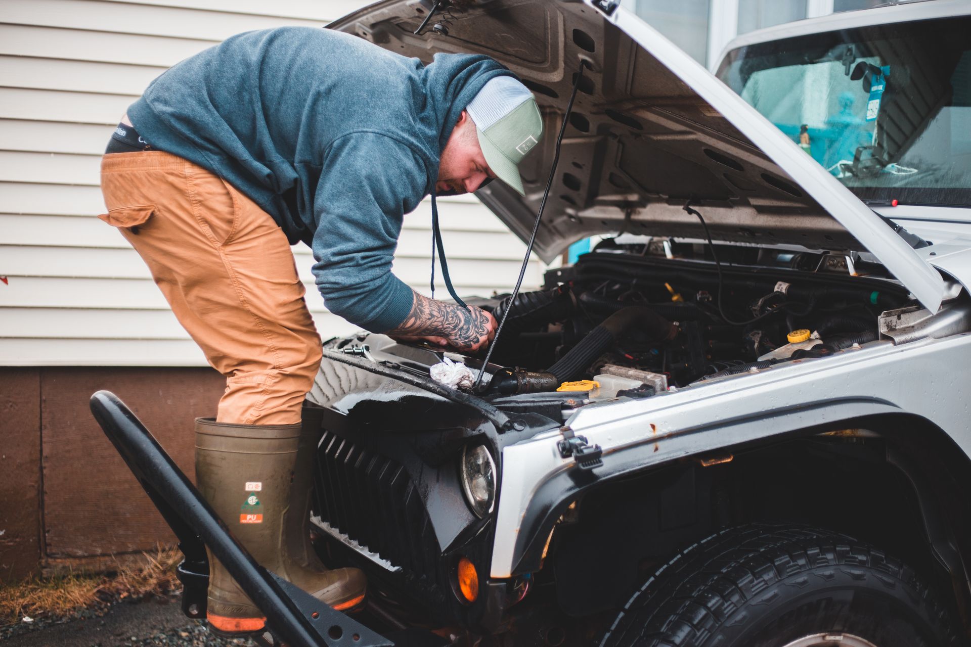 A man inspects and repairs a car engine outside, showcasing automotive maintenance and repair skills.