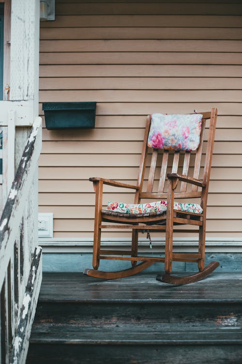 Aged rocking chair placed on withered wooden black porch near shabby white fence