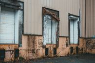 Facade of weathered building with dirty bright yellow wall and shabby closed windows