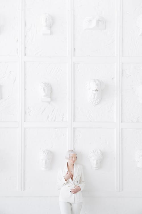 Albino Woman in a White Suit Standing on the Background of a White Wall with Sculptures 