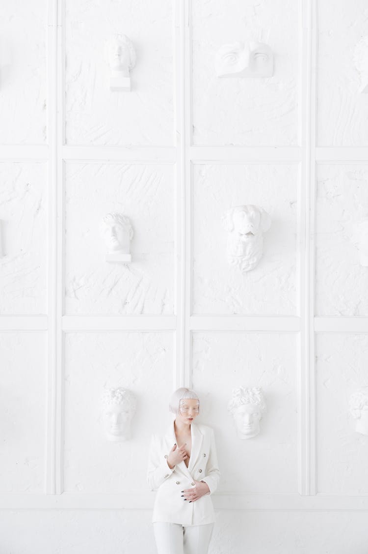 Albino Woman In A White Suit Standing On The Background Of A White Wall With Sculptures 