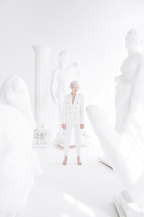 A Woman Wearing a White Suit Surrounded with Sculptures