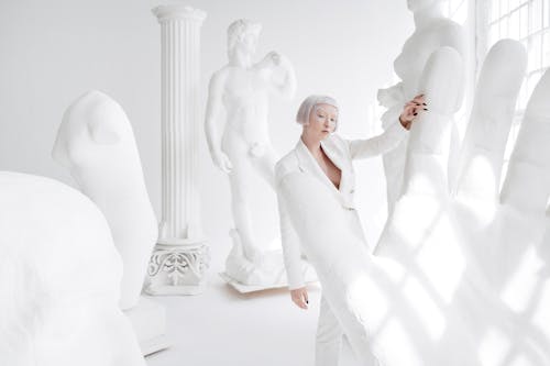 A Woman in a White Suit Holding on a Sculpture