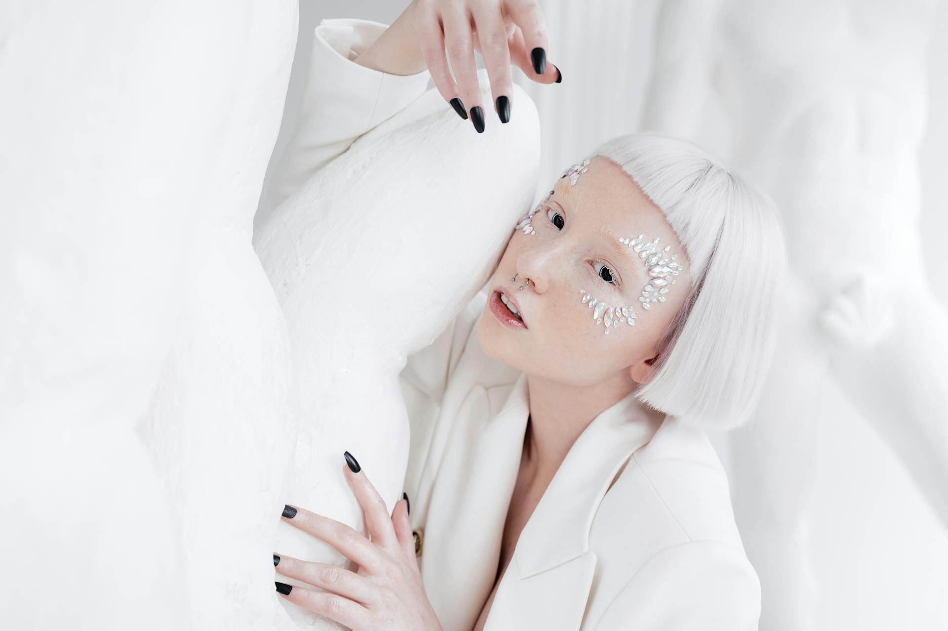 Creative portrait of a woman with face jewels and short hair, blending with a white artistic background.