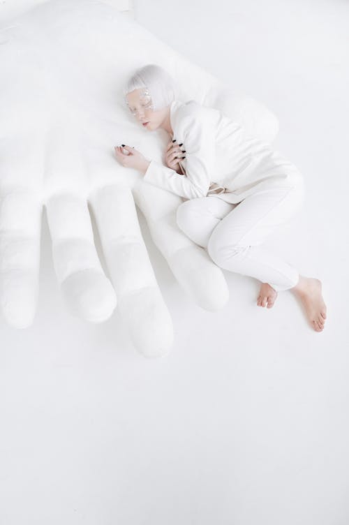 A Woman in a White Suit Lying on Hand Sculpture