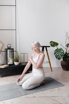 Serene woman with short hair practicing yoga in a minimalist indoor setting with natural decor.