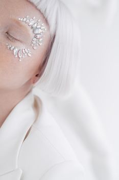 Close-up of woman with pearl-adorned eye makeup, white hair in a stylish pose.