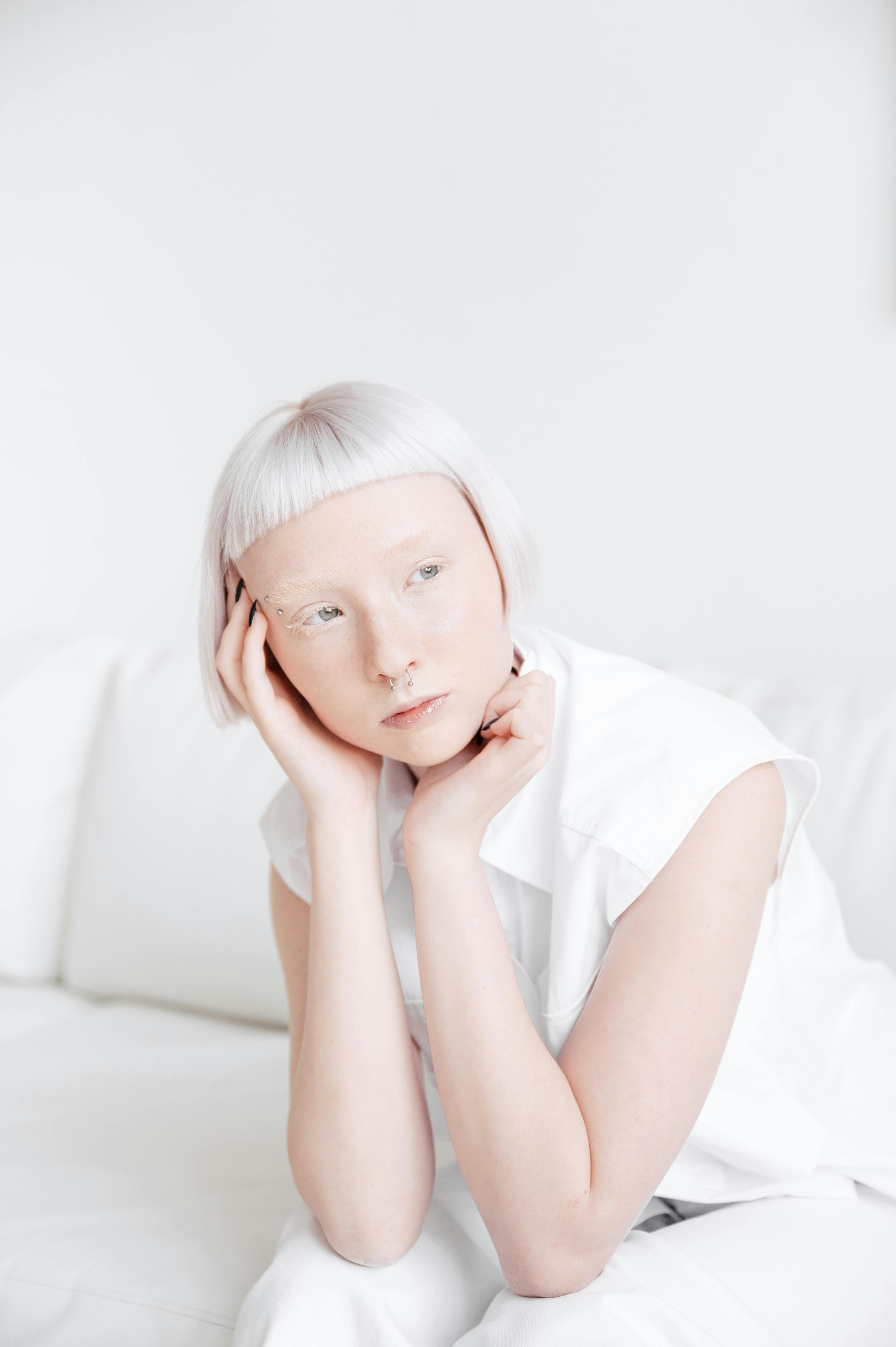 Young woman with short hair in a contemplative pose, dressed in white against a minimalist background.
