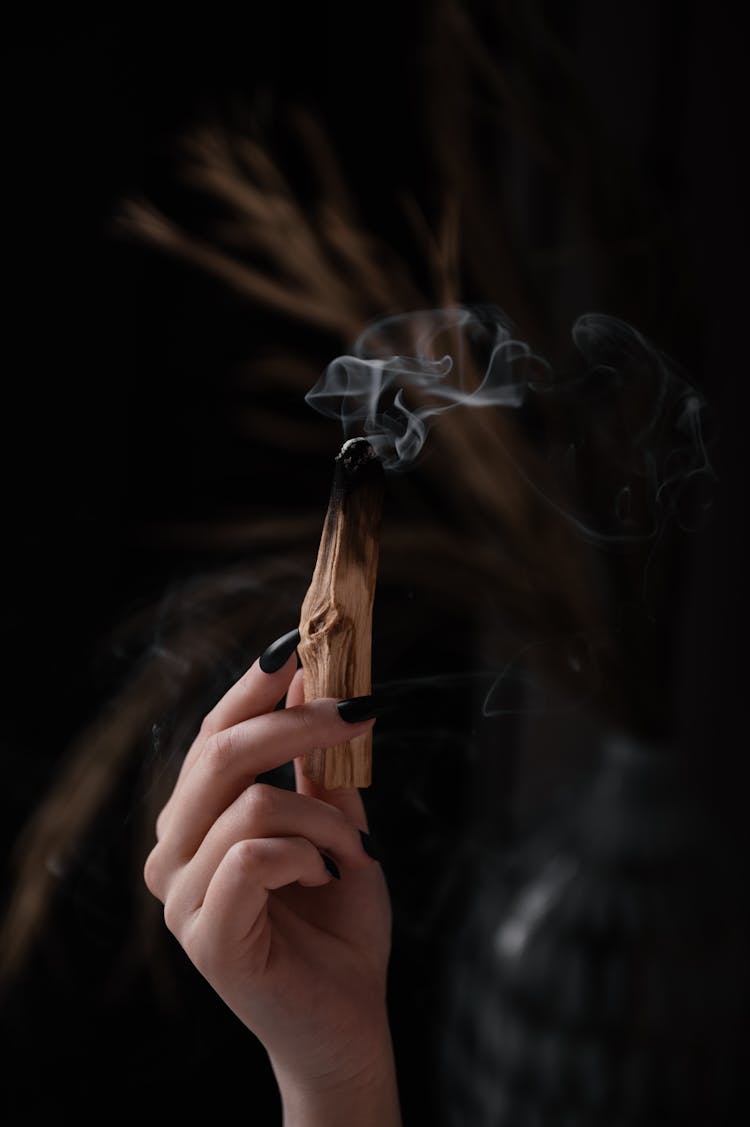 A Person Holding A Burnt Palo Santo With Smoke