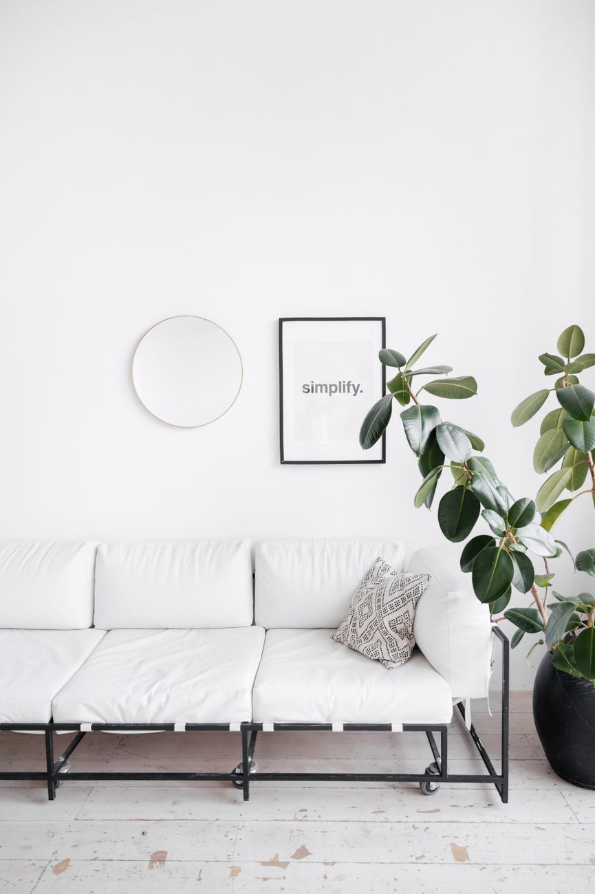 A bright minimalist living room featuring a white sofa, indoor plant, and wall decor creating a clean and serene space.. pexe