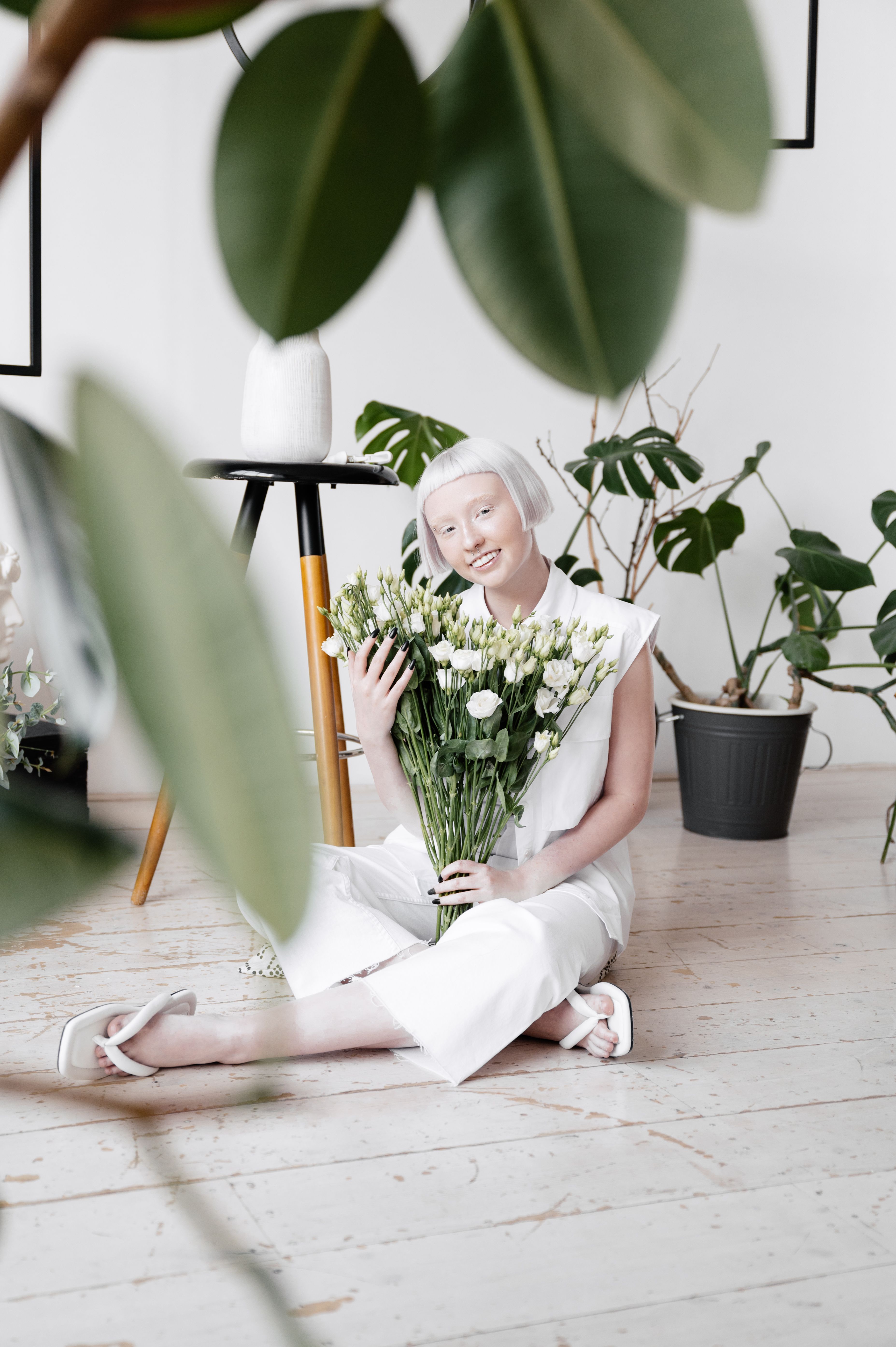 Woman in white outfit sitting with a bouquet of white flowers indoors.