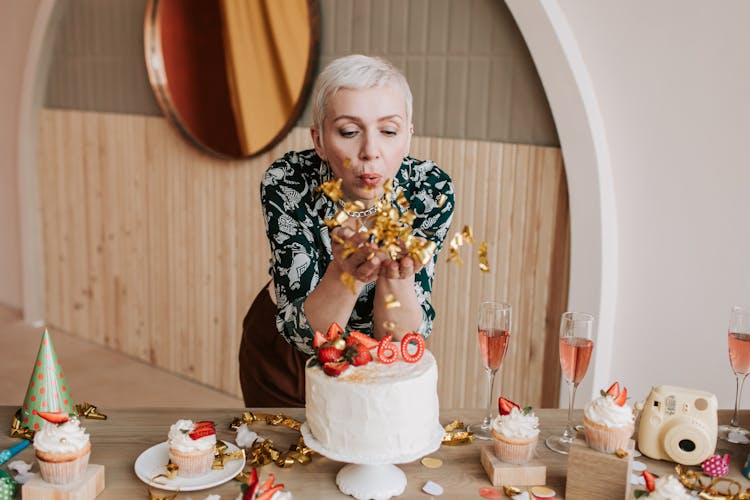 A Woman Blowing Gold Confetti Near A Cake