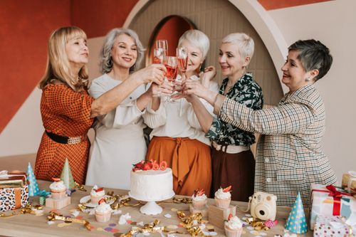 Free Senior women joyfully celebrating a birthday indoors with cake and drinks. Stock Photo