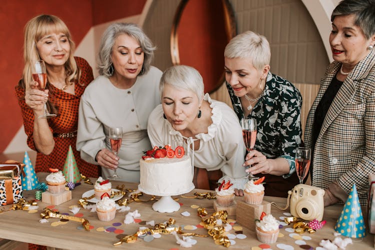 A Woman In A White Top Blowing The Candles On A Cake