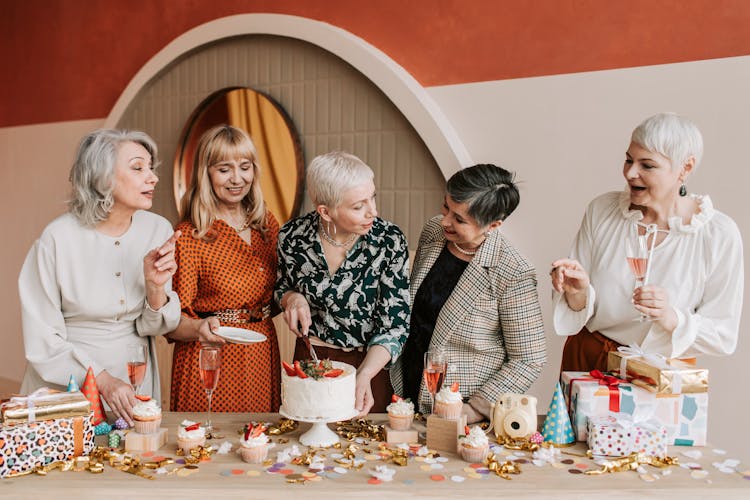 A Woman Slicing A Cake With Her Friends