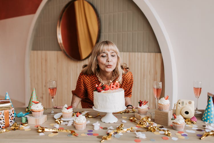 A Woman Blowing The Candles On A White Cake