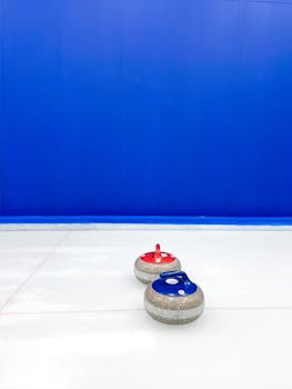 Close-up of red and blue curling stones on indoor ice rink against blue wall.