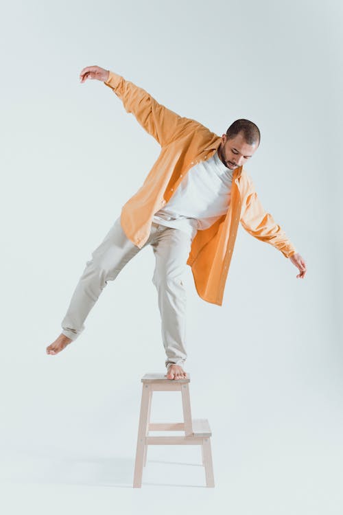 Man in Orange Long Sleeves Balancing on Step Stool 