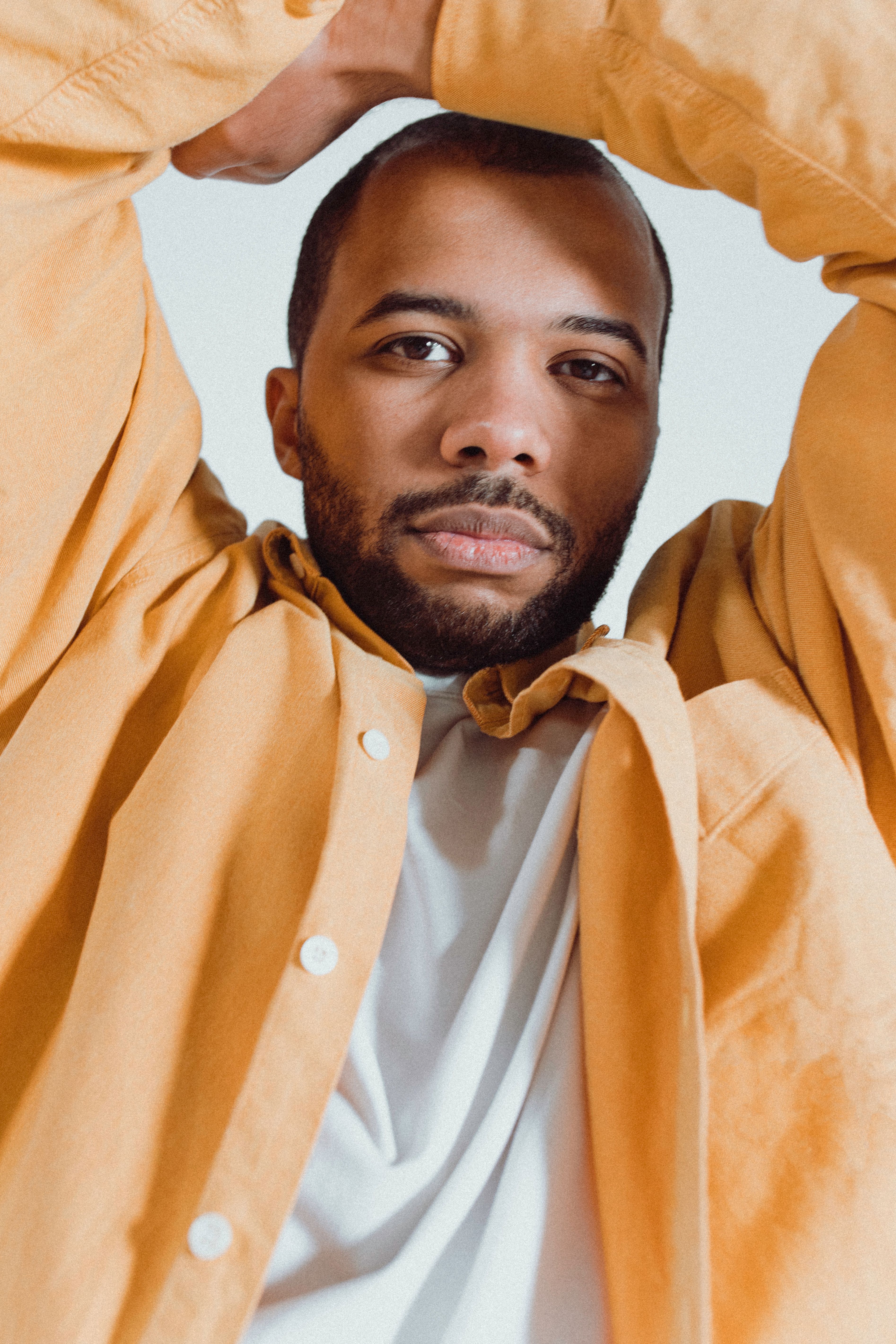 Portrait of a man in a yellow jacket against a neutral background, exuding confidence.