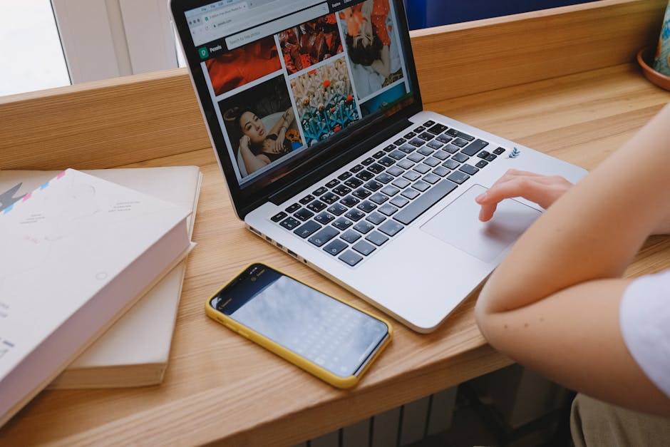 A person using a laptop at a wooden desk with a phone and notebooks nearby, ideal for remote work themes.