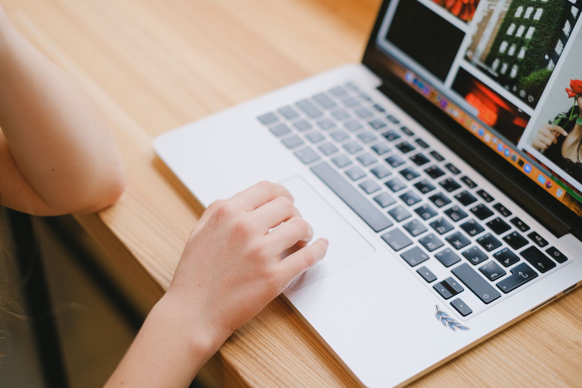Close-up view of a person's hand on a laptop touchpad, working on a wooden desk indoors.