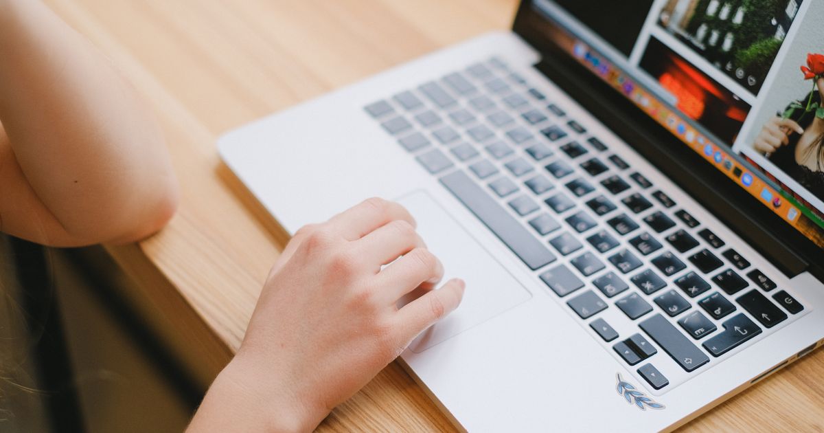 Close-up view of a person's hand on a laptop touchpad, working on a wooden desk indoors.