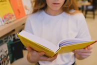 Woman in White Crew Neck T-shirt Holding White and Yellow Book