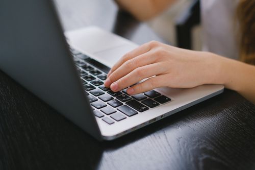 Free Close-up of a hand typing on a laptop keyboard placed on a wooden desk. Stock Photo