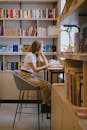 Woman Sitting on Gray Bar Stool while Studying in the Library