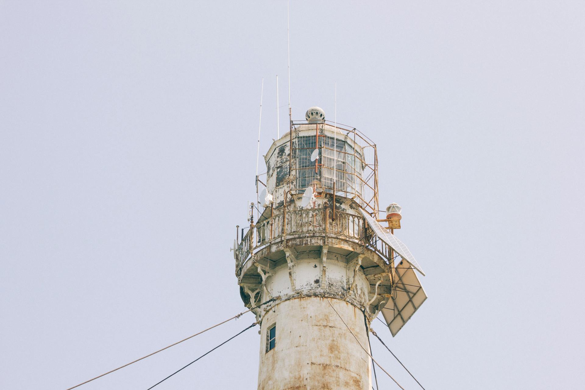 A close-up view of an old lighthouse tower featuring solar panels against a clear sky.