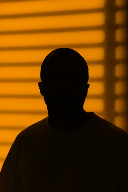 Dark silhouette of a man framed by yellow blinds creating a dramatic effect.