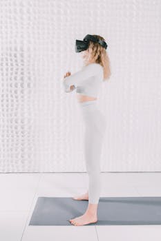 Blonde woman using VR headset for yoga on mat indoors, embracing technology and wellness.