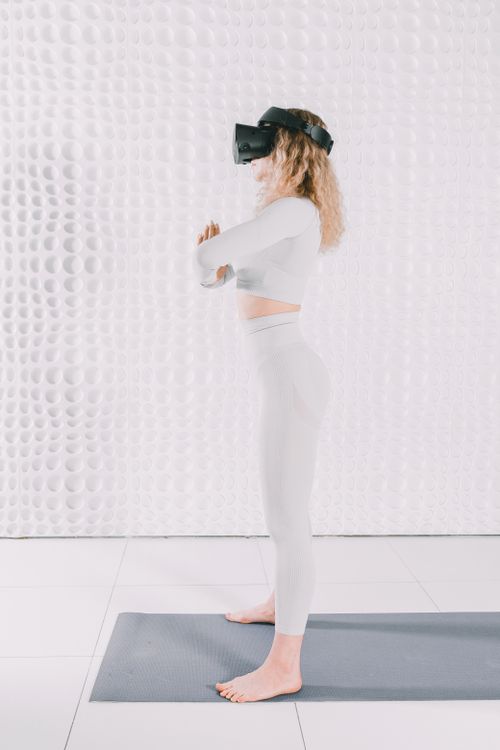 Free Blonde woman using VR headset for yoga on mat indoors, embracing technology and wellness. Stock Photo