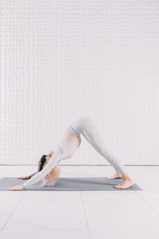 Adult woman doing downward dog yoga position indoors on a mat.