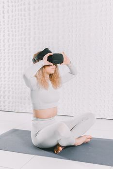 Woman wearing VR headset sitting cross-legged on yoga mat in a modern indoor setting.
