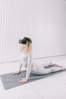 Woman practicing upward facing dog yoga pose with VR goggles indoors on a mat in a minimalist setting.