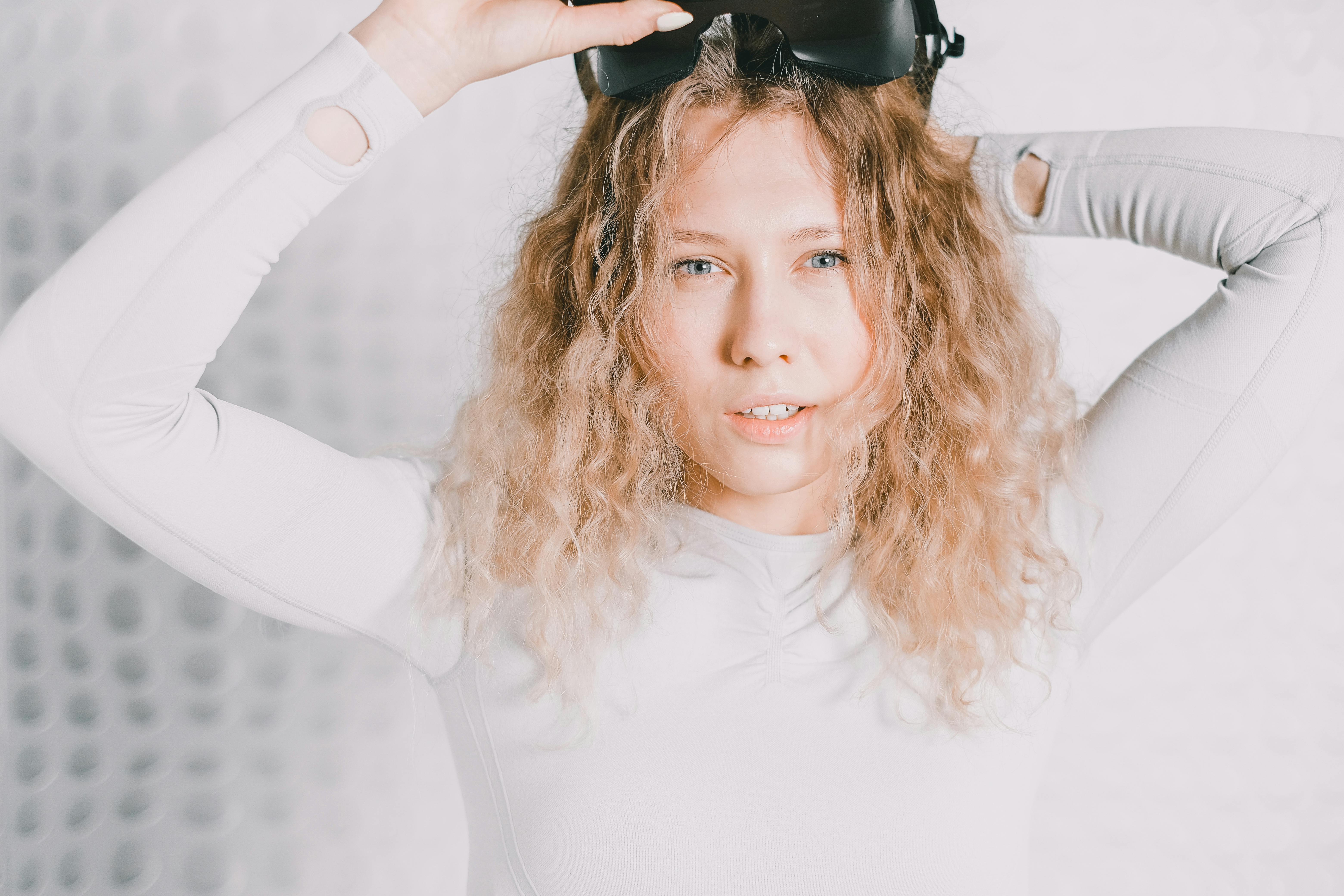 A woman with curly blonde hair holding a VR headset in a modern setting.